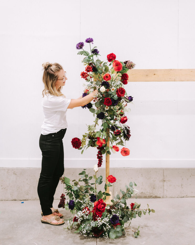 The owner is creating a floral arch piece and ground arrangement using red and purple flowers.